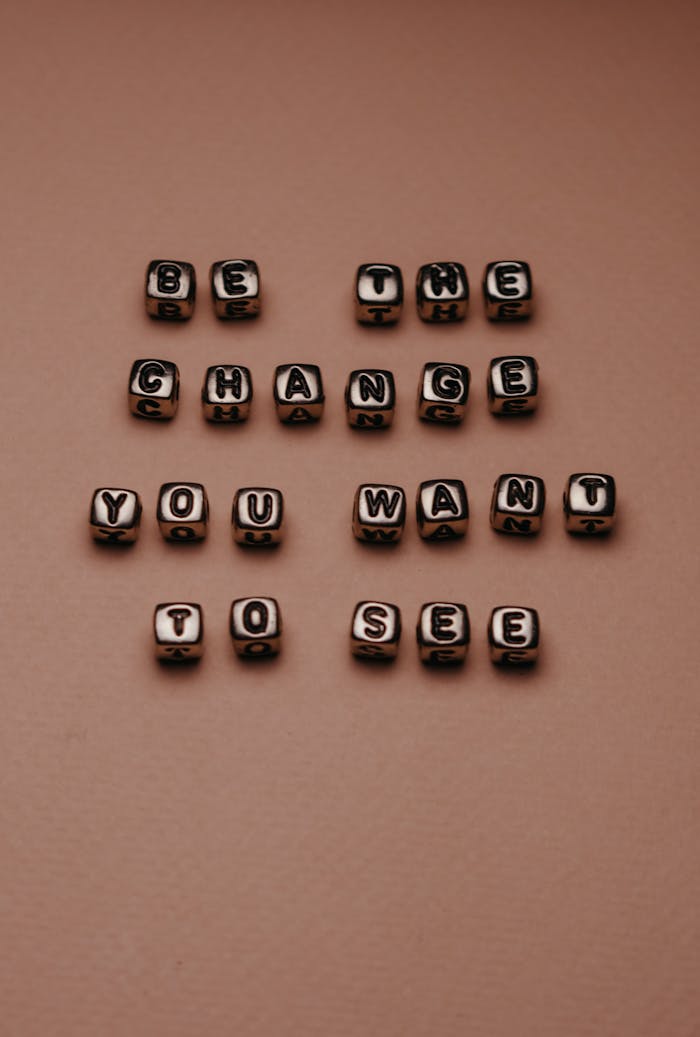 Inspirational quote 'Be the change you want to see' with letter beads on a neutral background.